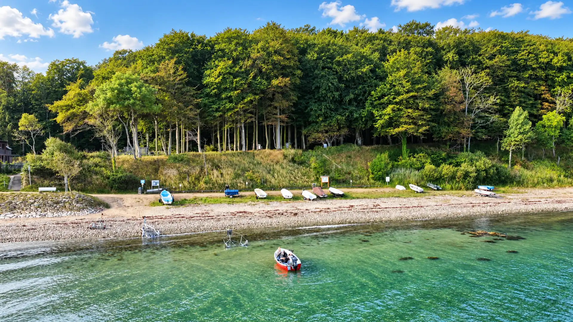 Vereinsgelände am Eitz: Kleinboote am Strand vor dem Buchenwald, ein rotes Boot im klaren Ostseewasser